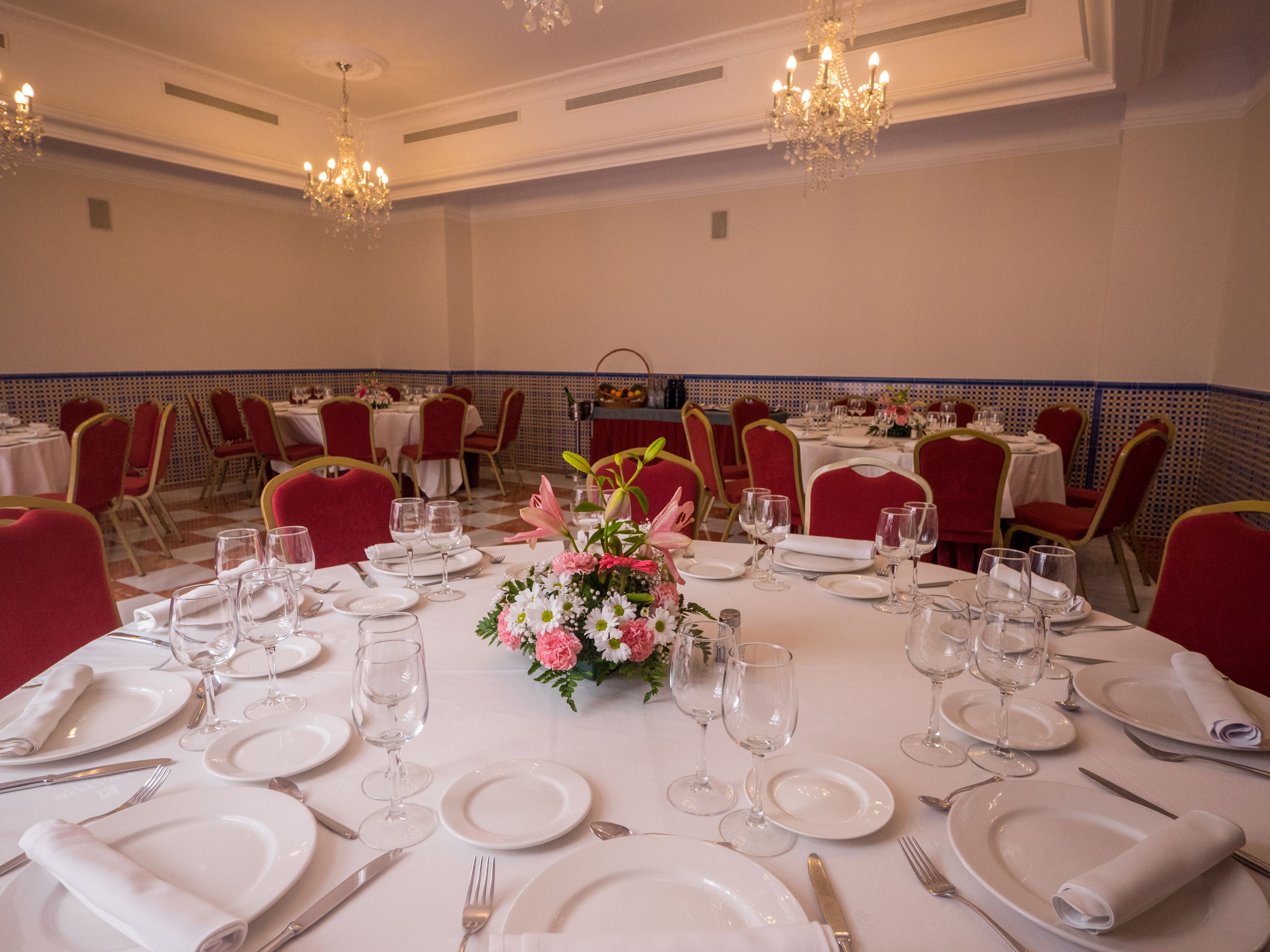 Une salle de banquet avec des tables rondes dressées pour le repas, des chaises rouges et des lustres.