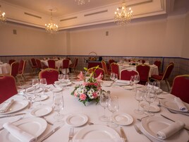 Ein Festsaal mit runden Esstischen, roten Stühlen und Kristallleuchtern.