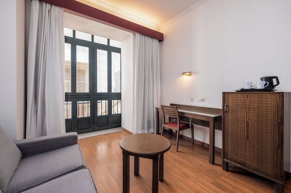 Una habitación con sofá, una mesa redonda, una silla, un armario y una ventana con cortinas.