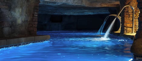 An indoor swimming pool with a waterfall feature, surrounded by stone walls.