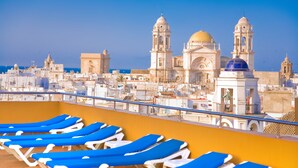 A rooftop with blue lounge chairs and a view of historic buildings with domes and bell towers. - Senator Cadiz Hotel (Cádiz)