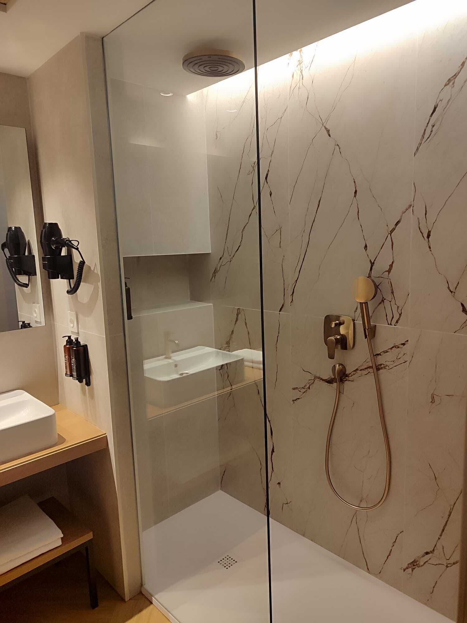 Un baño moderno con ducha envuelta en vidrio, un lavamanos blanco y un espejo.