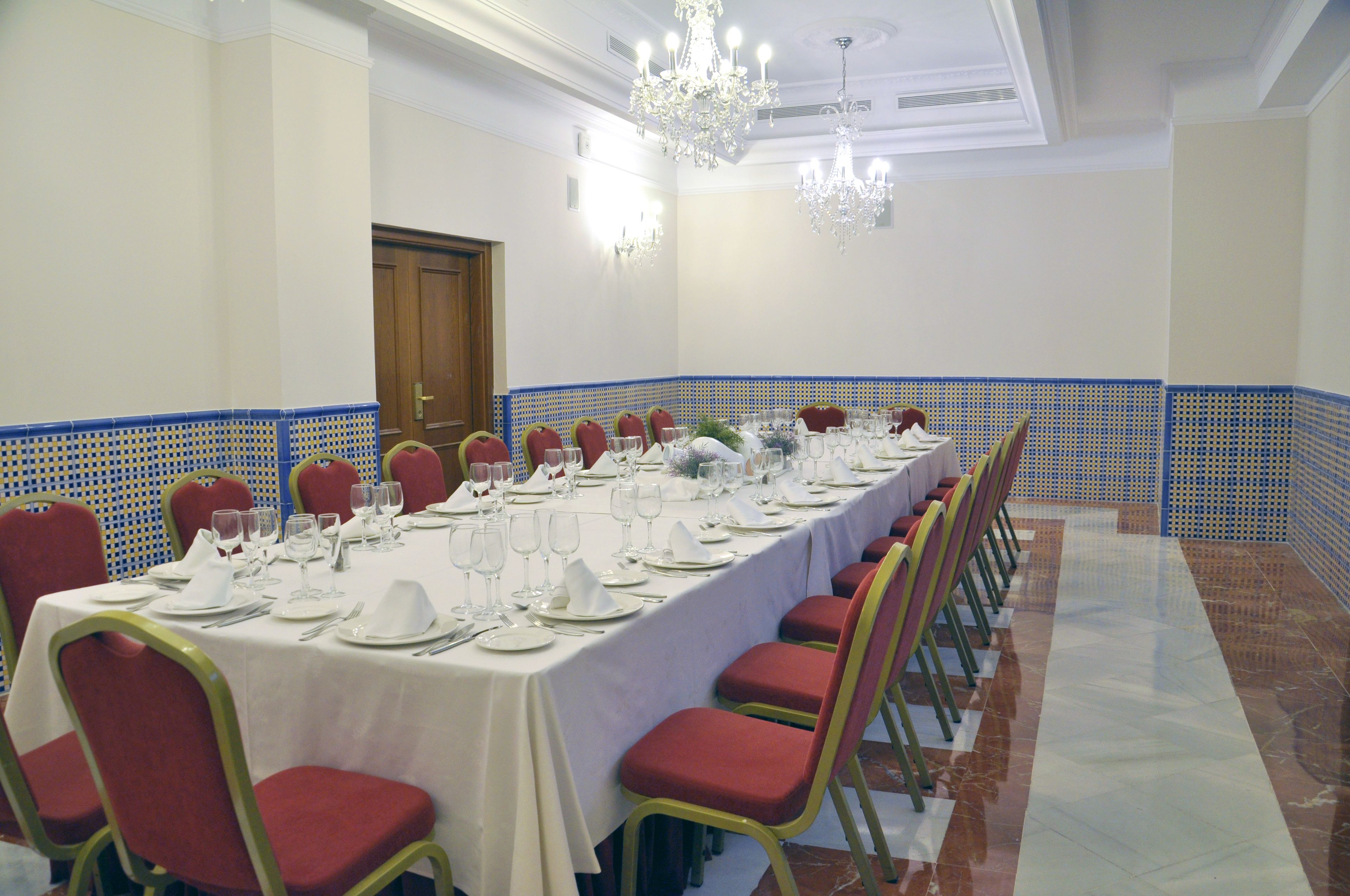 Una larga mesa de banquete dispuesta para un evento formal, con sillas rojas y manteles blancos.