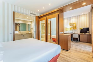 A hotel room with a large bed, a desk with a chair, a television, and a bathroom visible through an open door.
