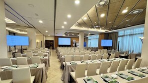 A conference room with rows of tables and chairs, equipped with presentation screens and a projector. - Sercotel Las Artes Pinto (Pinto)
