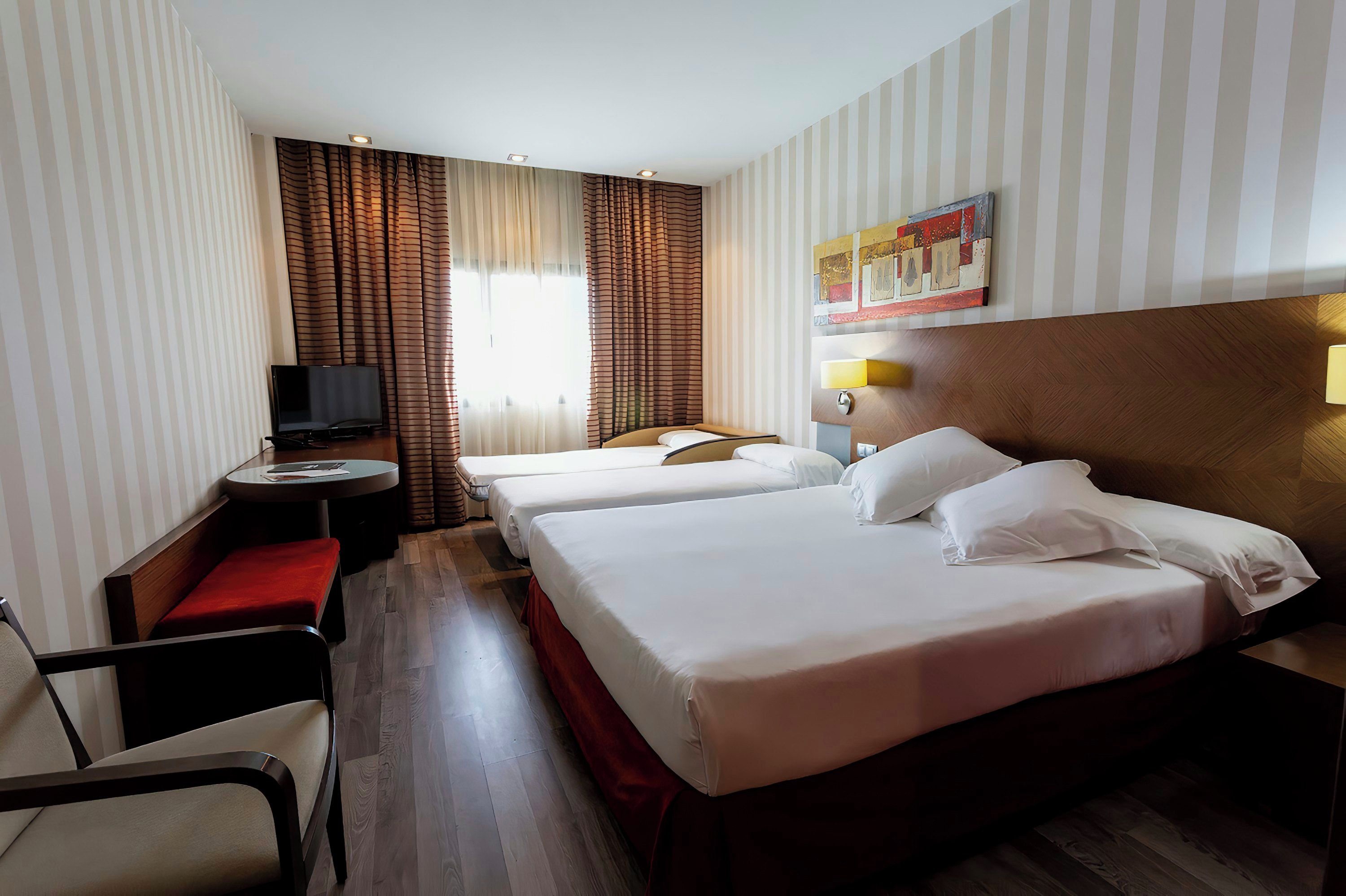 Habitación de hotel con dos camas, un escritorio, una silla, un televisor y una ventana con cortinas.