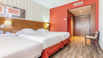 Habitación de hotel con dos camas, cabecero de madera, pared de acento roja, una silla y una puerta que da a otra habitación.
