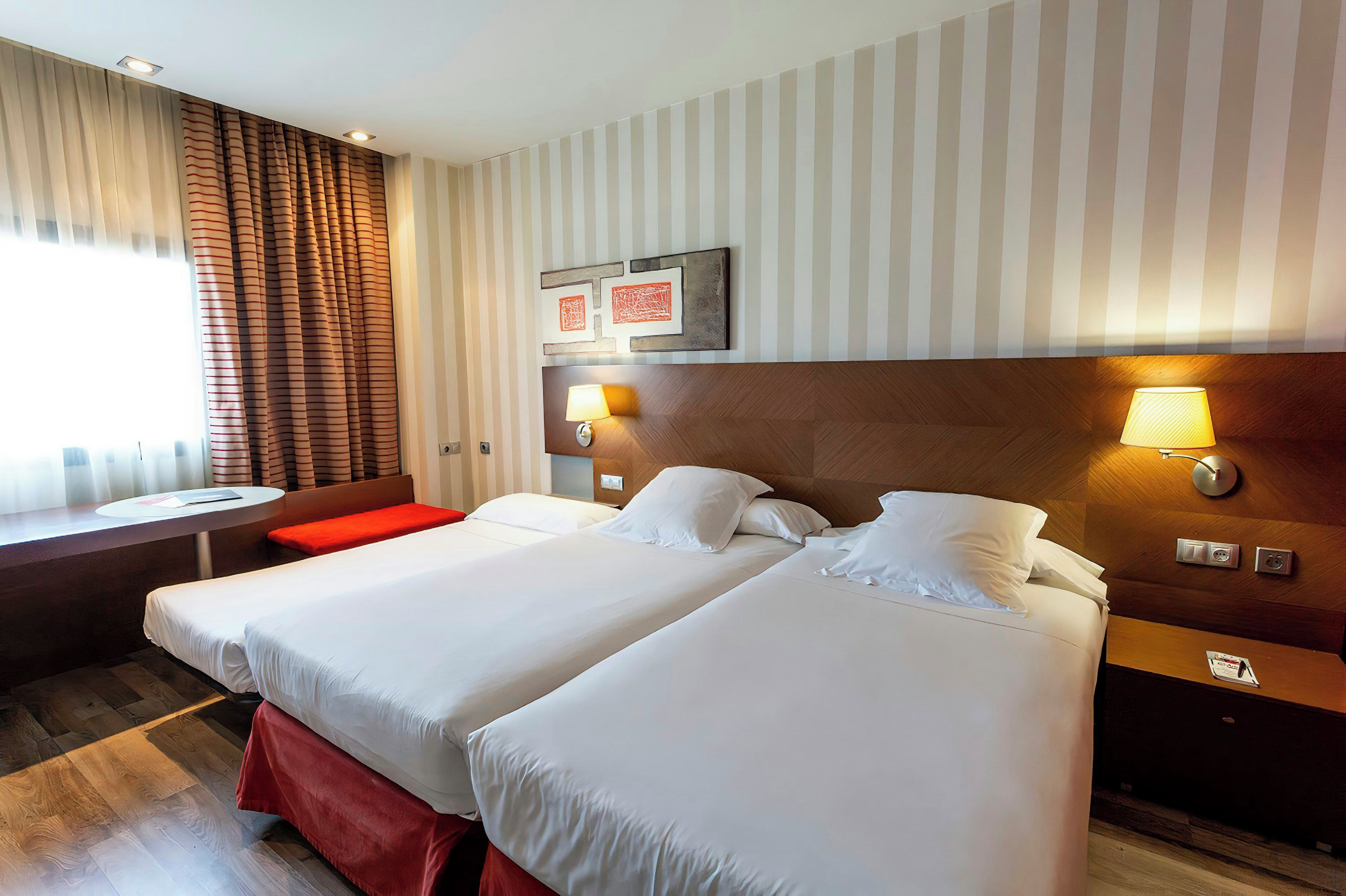 Une chambre d’hôtel avec deux lits, une petite table et un banc.