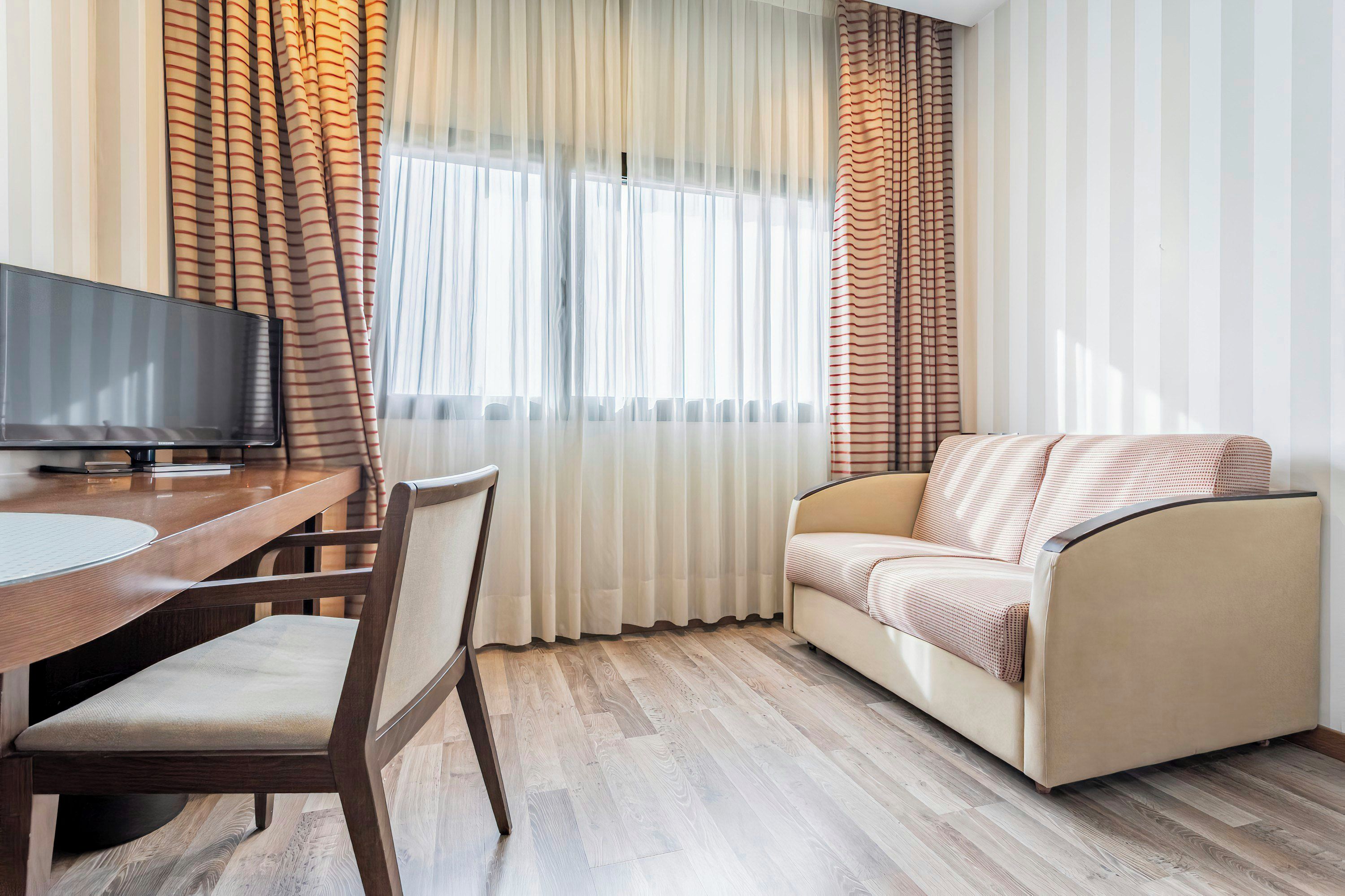Una sala de estar moderna con un sofá, una mesa de comedor con sillas, un televisor de pantalla plana y cortinas traslúcidas con estampado a rayas.