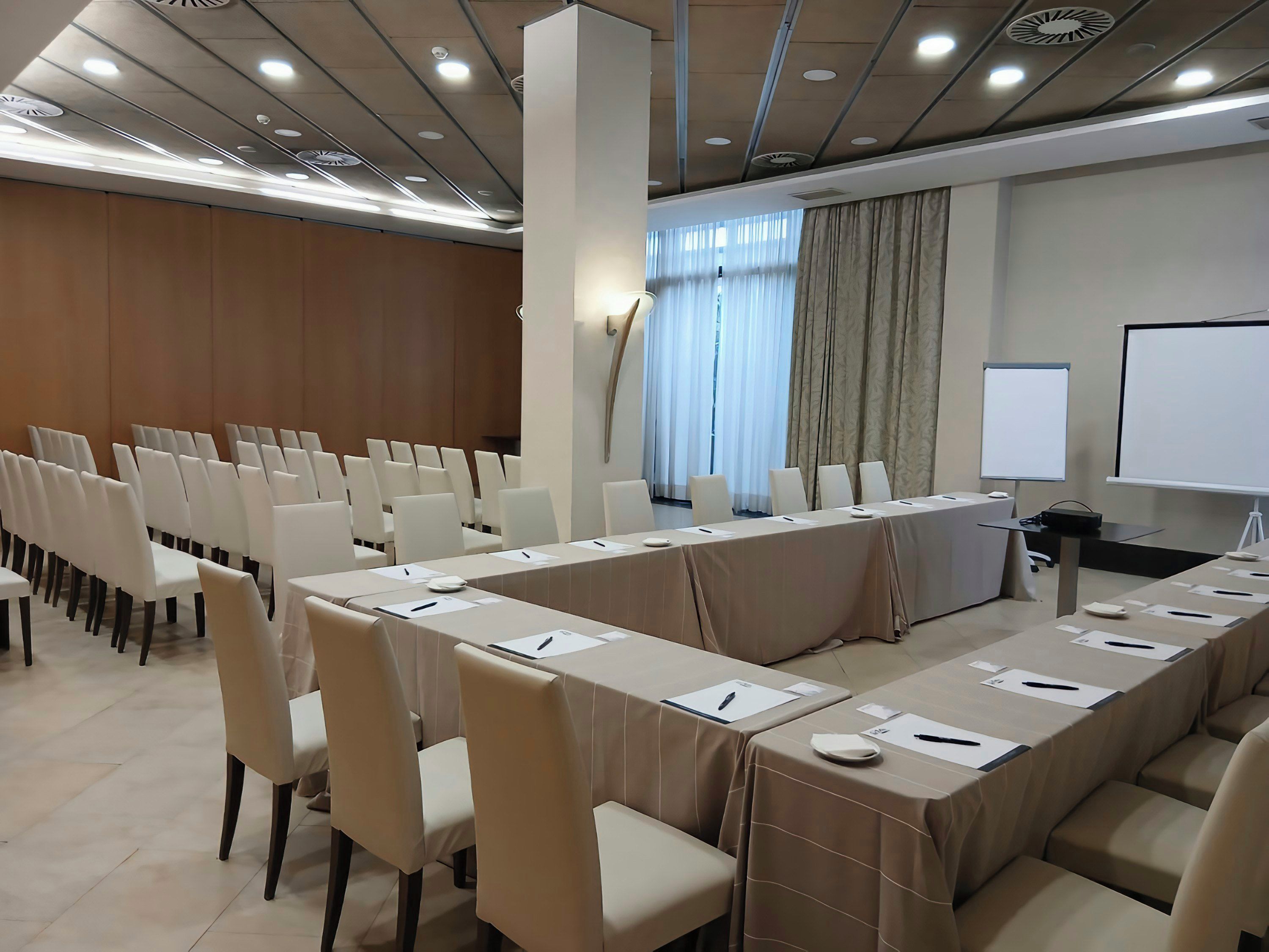 Ein Konferenzraum mit einem langen Tisch, Stühlen, einer Projektionsleinwand und einer Whiteboard-Tafel.