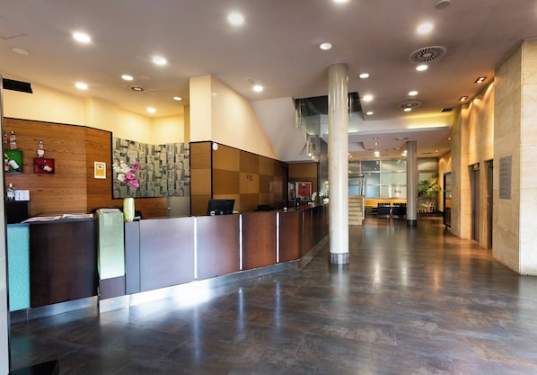 Un área de recepción moderna con un mostrador de madera, un separador de vidrio y piso de mármol.