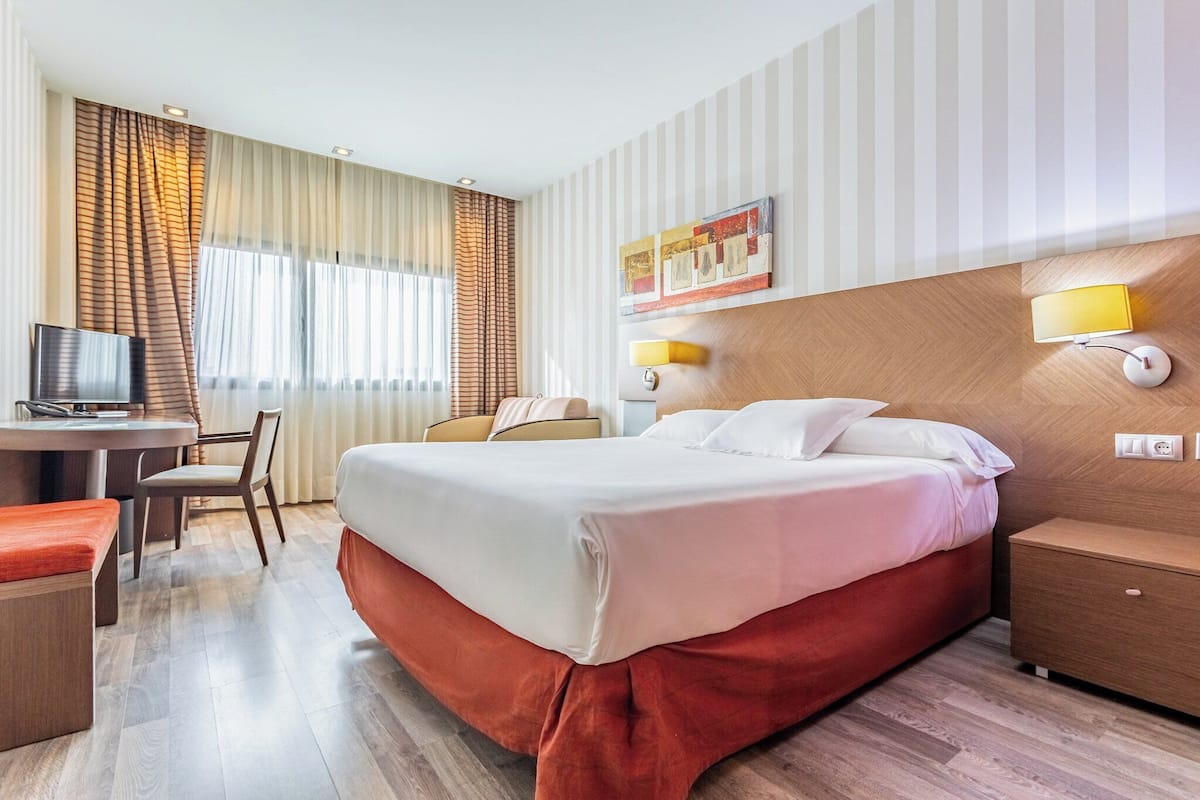 Una habitación de hotel con una cama, un escritorio, una silla y un televisor.