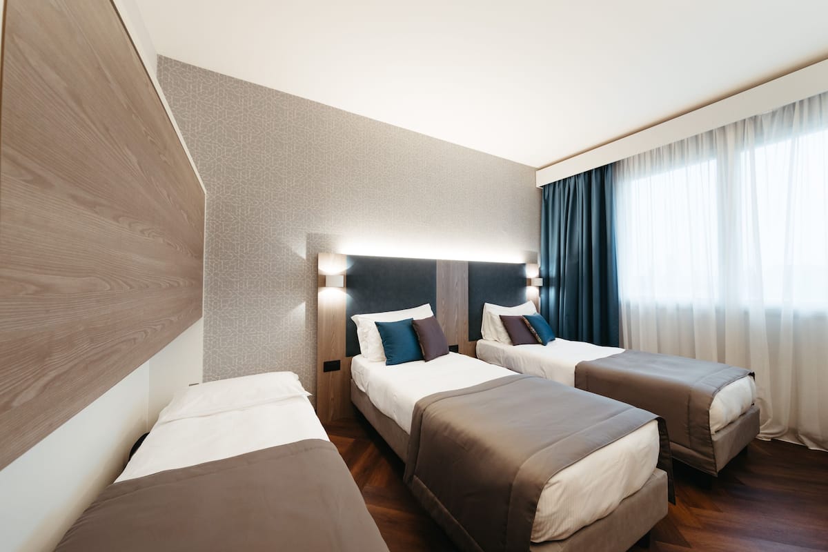 A hotel room with two beds, a large window with curtains, and a modern design.