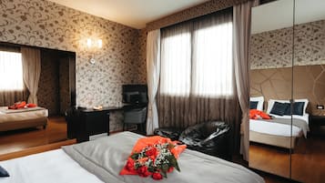 Habitación de hotel con cama, escritorio, silla, televisor y un espejo grande.