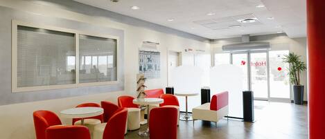 A modern lobby with red and white seating, a large window, and a reception area.