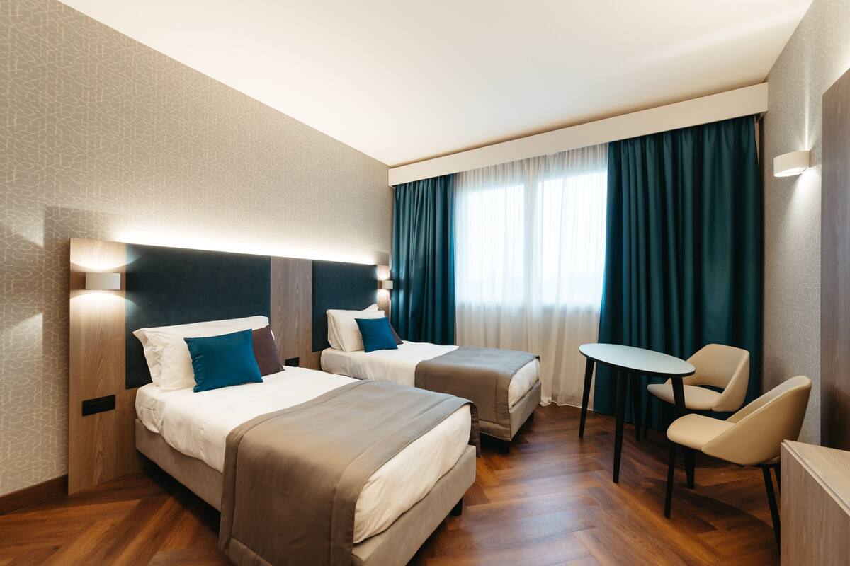 A hotel room with two beds, a small table, and a chair.