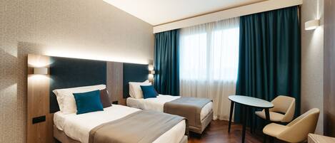 Habitación de hotel con dos camas, una mesita y una silla.