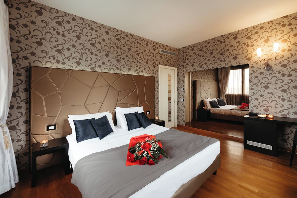 A hotel room with a large bed, a nightstand, a desk, and a mirror.