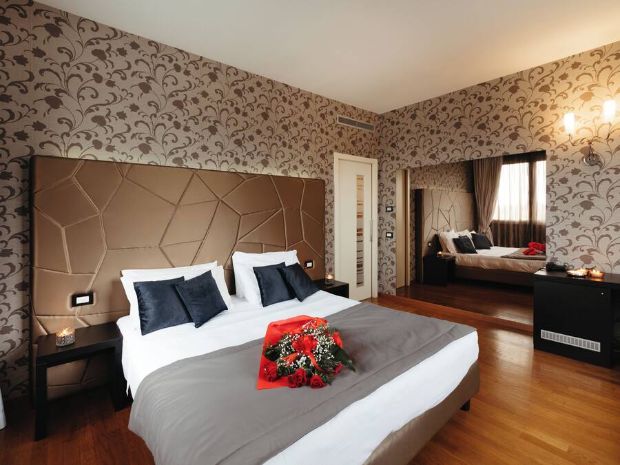 A hotel room with a large bed, a nightstand, a desk, and a mirror.