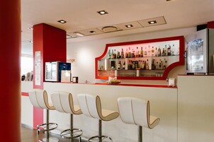 Uma área de bar com uma parede vermelha de destaque, diversos frascos de bebidas e banquetas modernas.