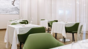 A restaurant with multiple tables, each set with white tablecloths and green chairs.