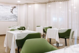 Restaurante com várias mesas, cada uma com toalhas brancas e cadeiras verdes.