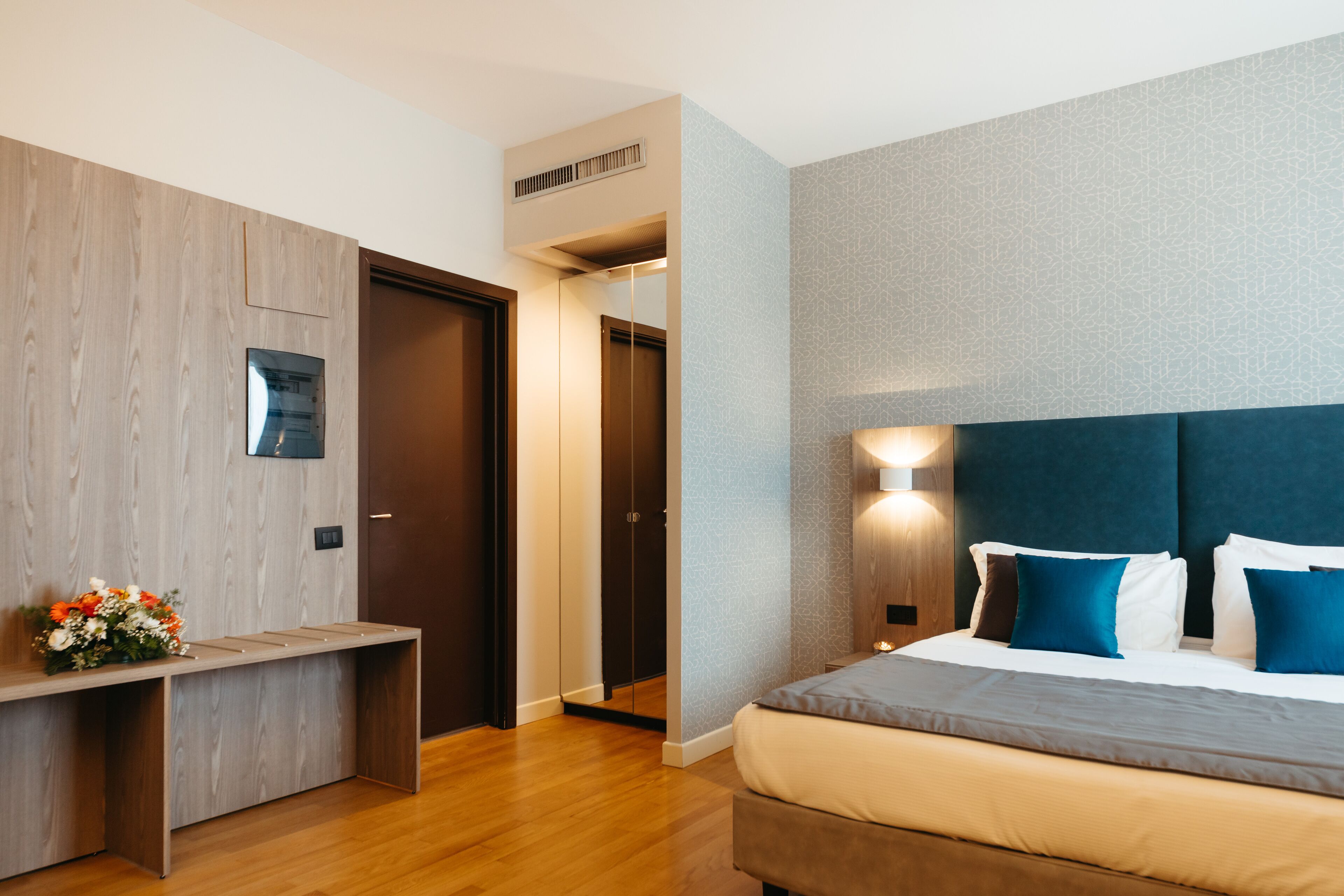 A modern hotel room with a wooden desk, a bed with blue and white bedding, and a patterned wall.