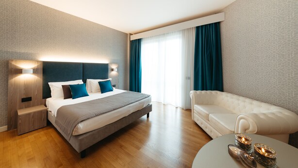 A modern hotel room with a large bed, a white sofa, and a round coffee table.