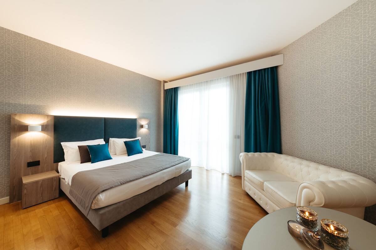 A modern hotel room with a large bed, a white sofa, and a round coffee table.