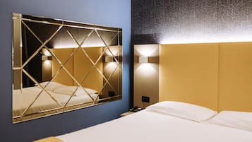 Una camera d'albergo con uno specchio grande, un letto con lenzuola bianche, un comodino con il telefono e un punto luce a parete.
