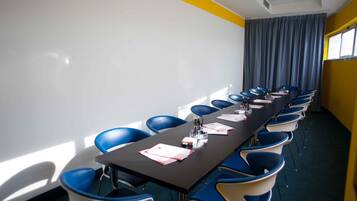 A conference room with a long table, blue chairs, a whiteboard, and a window with curtains.
