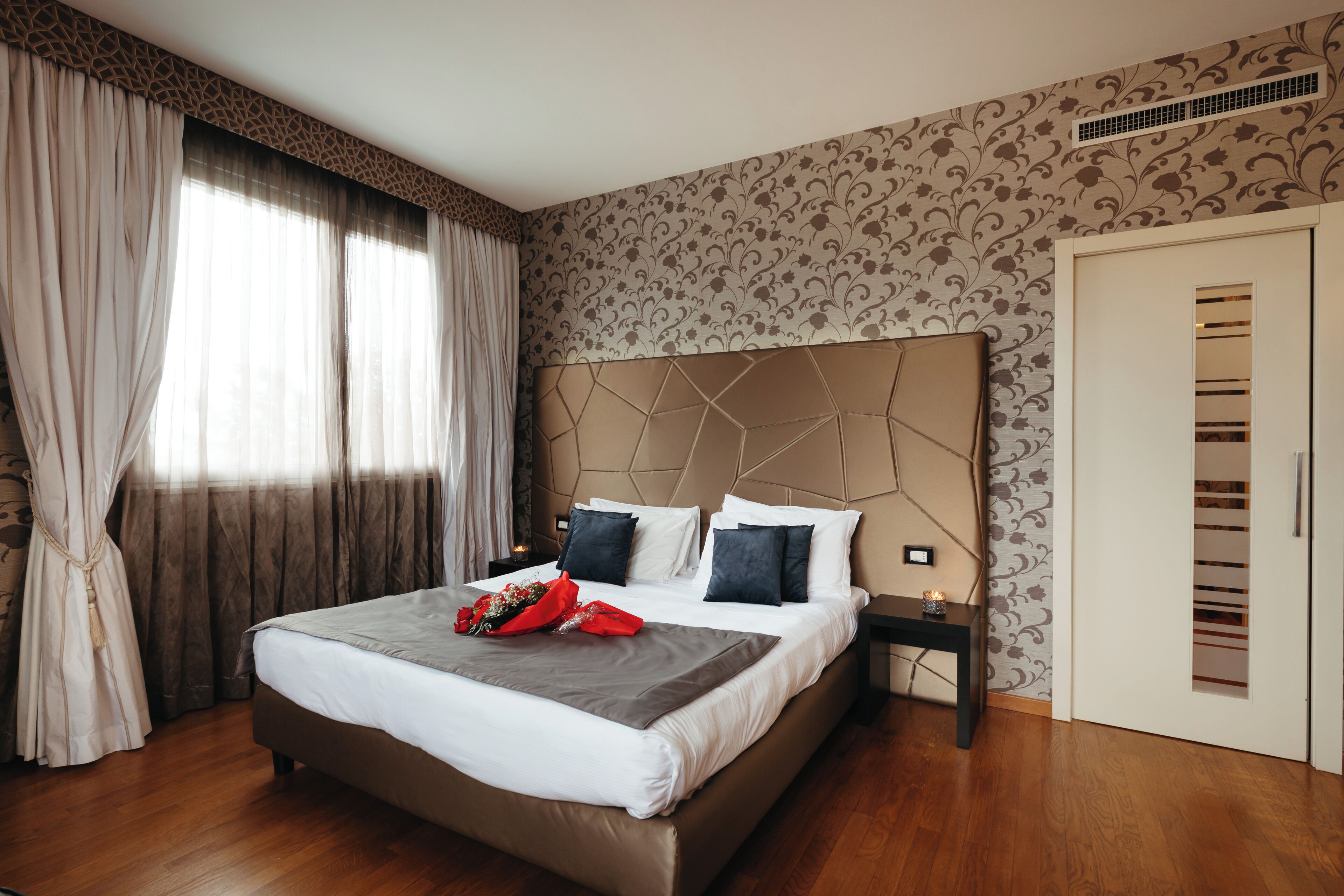 A modern hotel room with a large bed, a nightstand, a wardrobe, and a window with curtains.