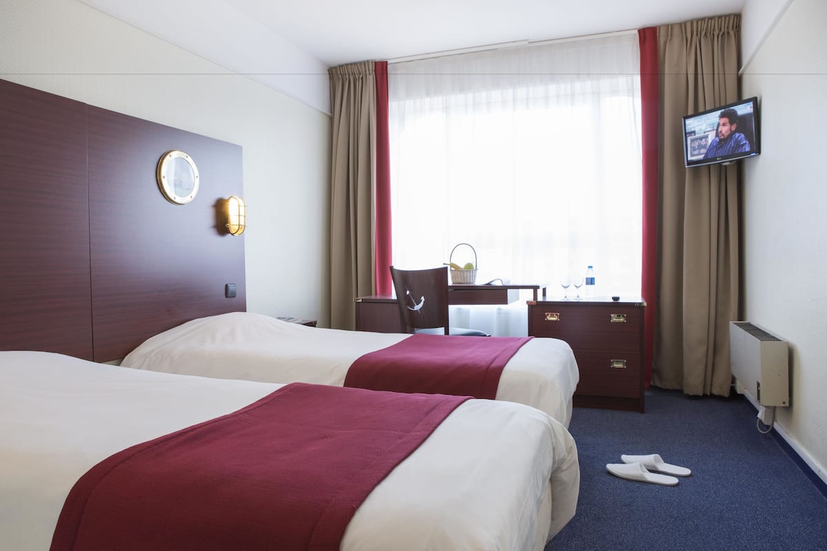 A hotel room with two beds, a desk, a chair, a television, and a window with curtains.