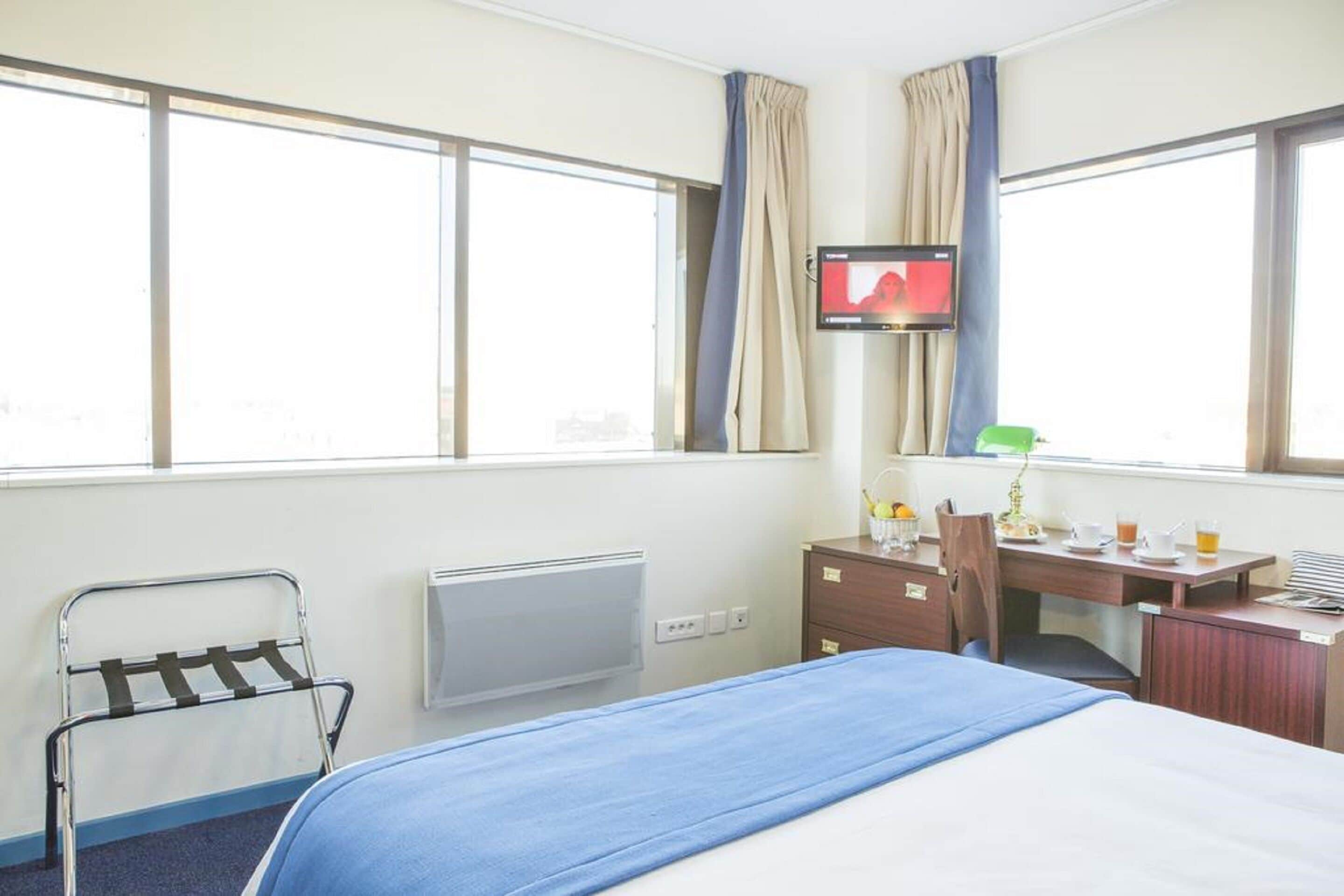 Una habitación de hotel con cama, escritorio, silla, televisión y ventana.
