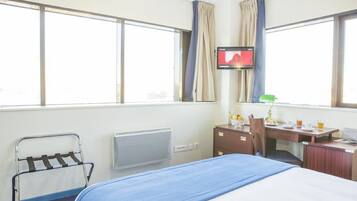 Una habitación de hotel con cama, escritorio, silla, televisión y ventana.