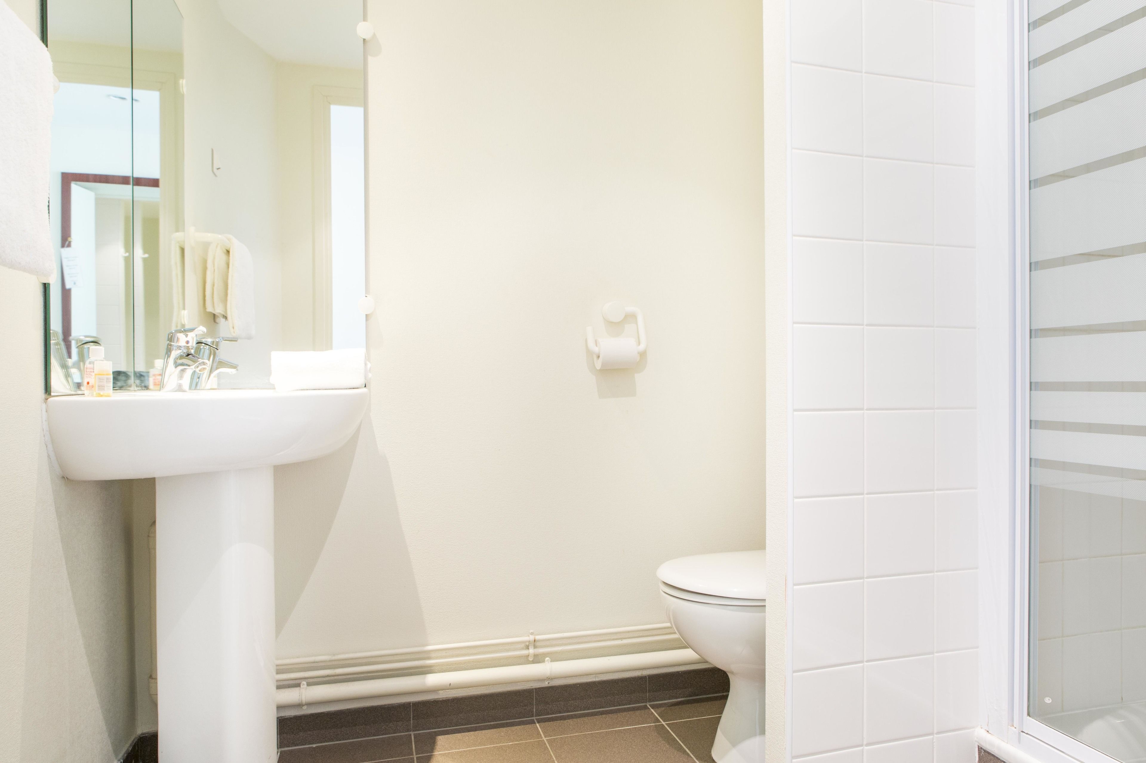 Un baño con lavamanos, espejo y retrete blancos.