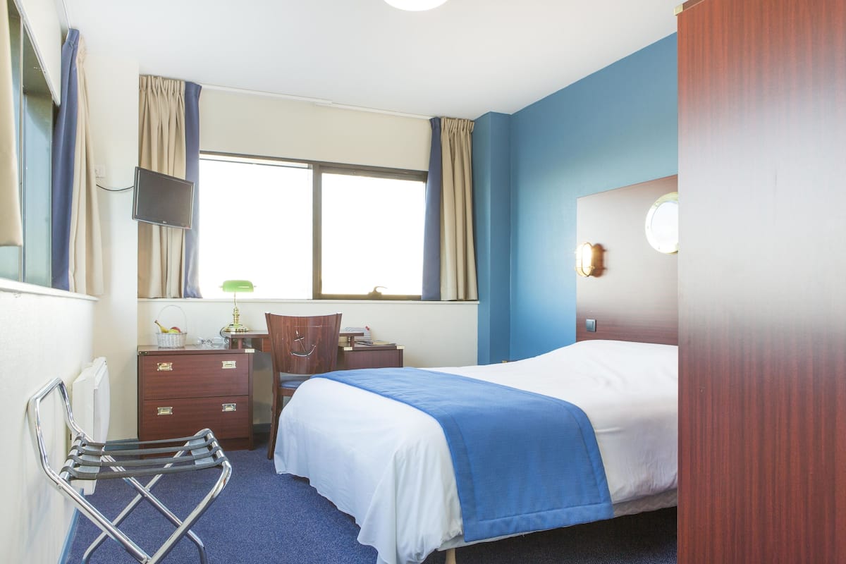 A hotel room with a bed, a desk with a lamp, a chair, and a window with curtains.