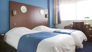 A hotel room with two beds, a wooden headboard, a desk with a chair, and a window with curtains. - Les Gens de Mer Dunkerque (Dunkirk)