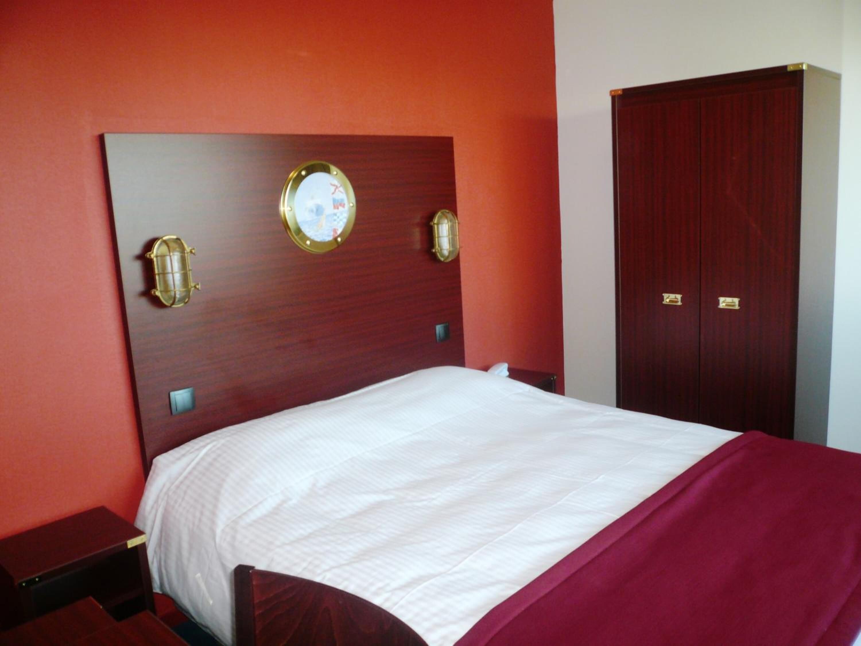 Ein Hotelzimmer mit einem hölzernen Kopfende, einem Bett mit weißer Bettwäsche, einer roten Wand und einem Holzschrank.