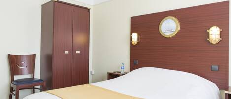 Una habitación de hotel con una cama grande, un armario de madera, una silla y una mesita de noche con una botella de agua.