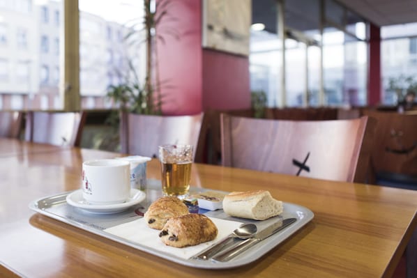 A tray with a cup, a glass of beer, and two pastries on a wooden table in a cafe.