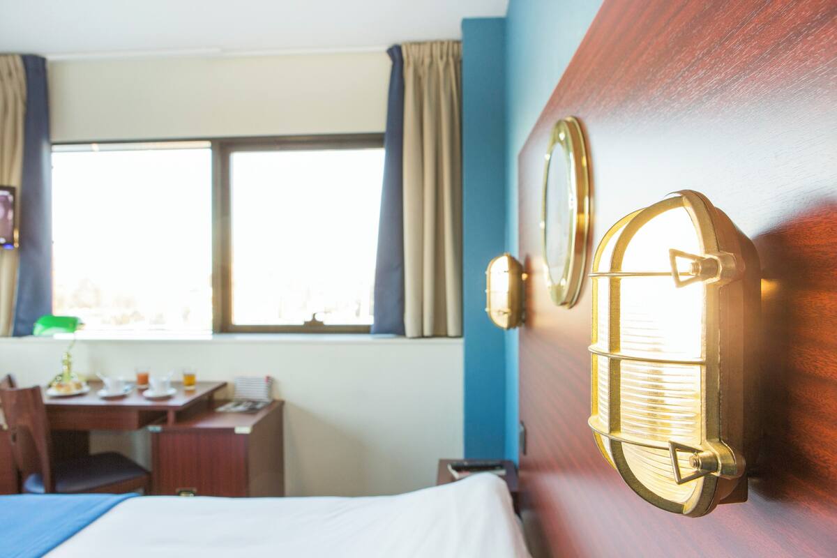 A hotel room with a bed, a desk, and a window with curtains.
