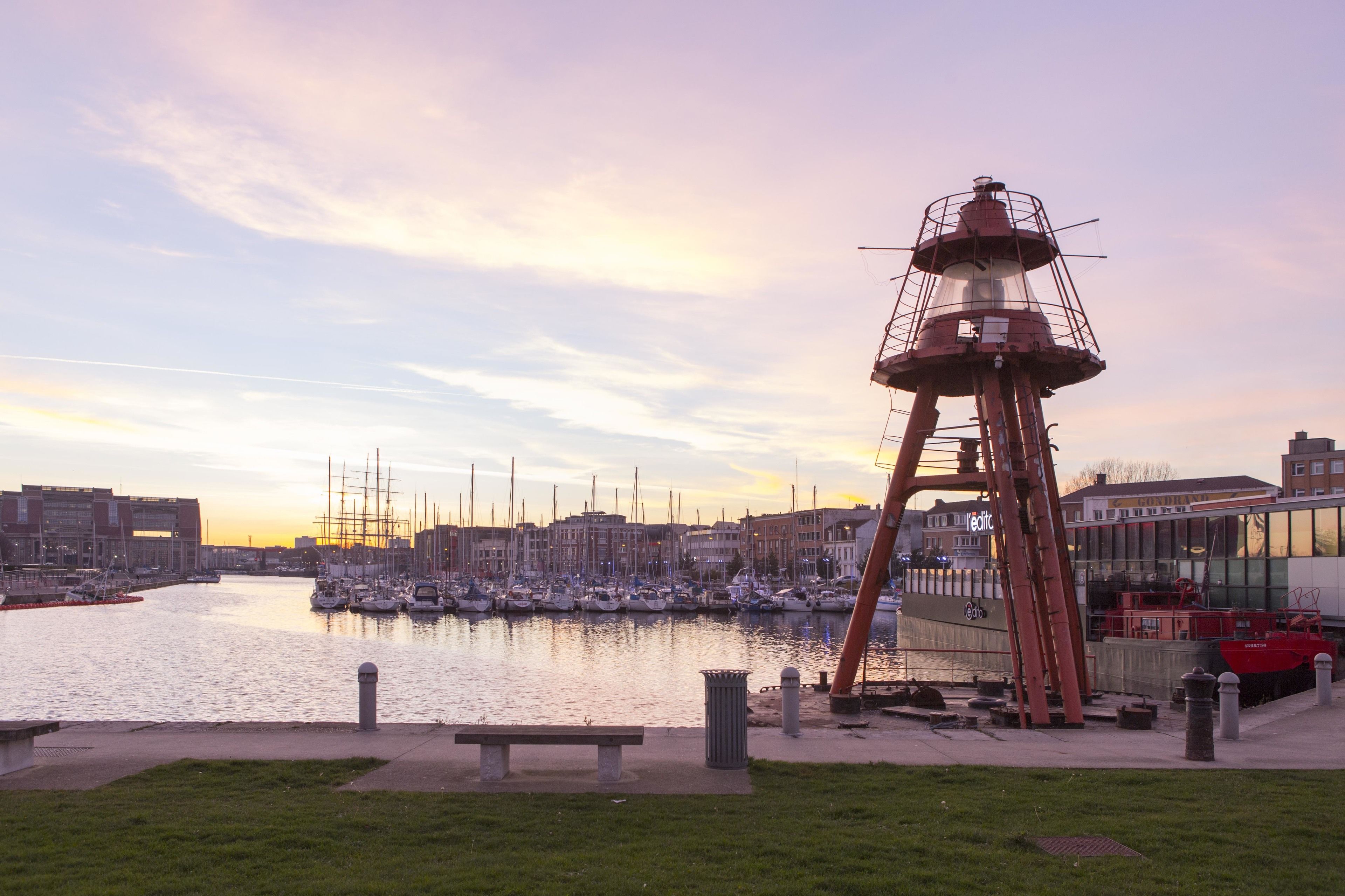 Un puerto deportivo con barcos, un faro y edificios al fondo.