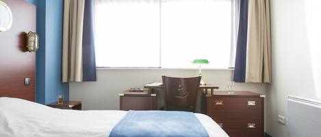 A hotel room with two beds, a desk, a chair, and a window with curtains.