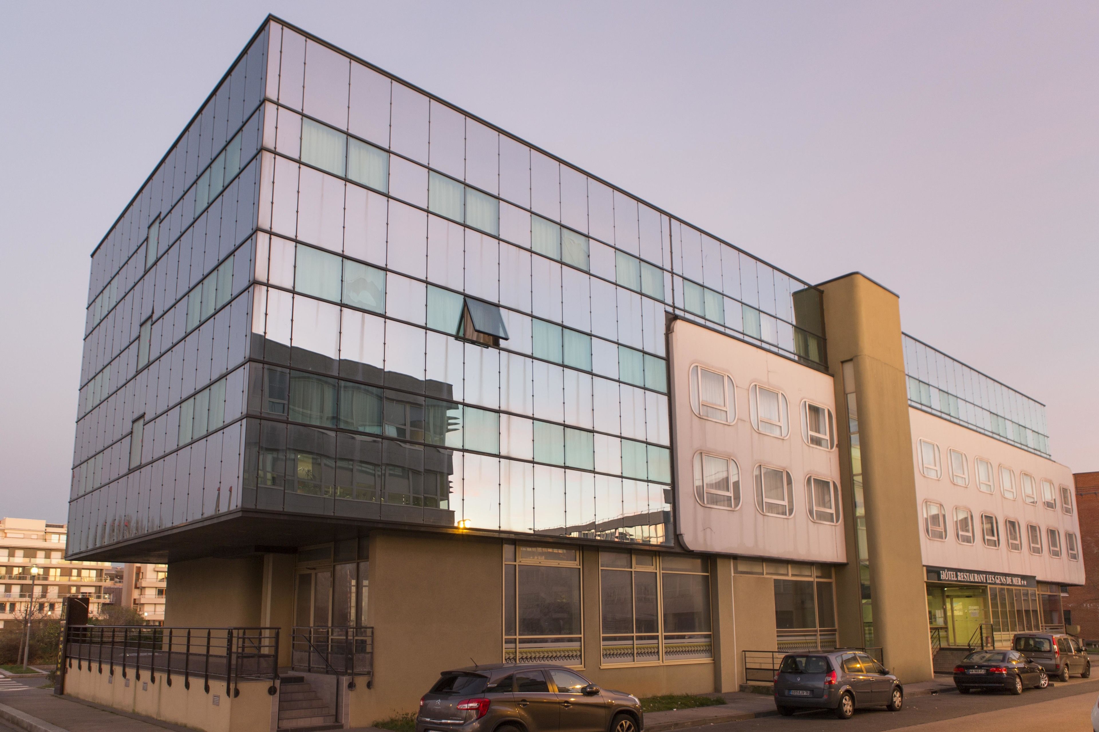 A modern building with a glass facade, a flat roof, and a sign for a hotel restaurant.