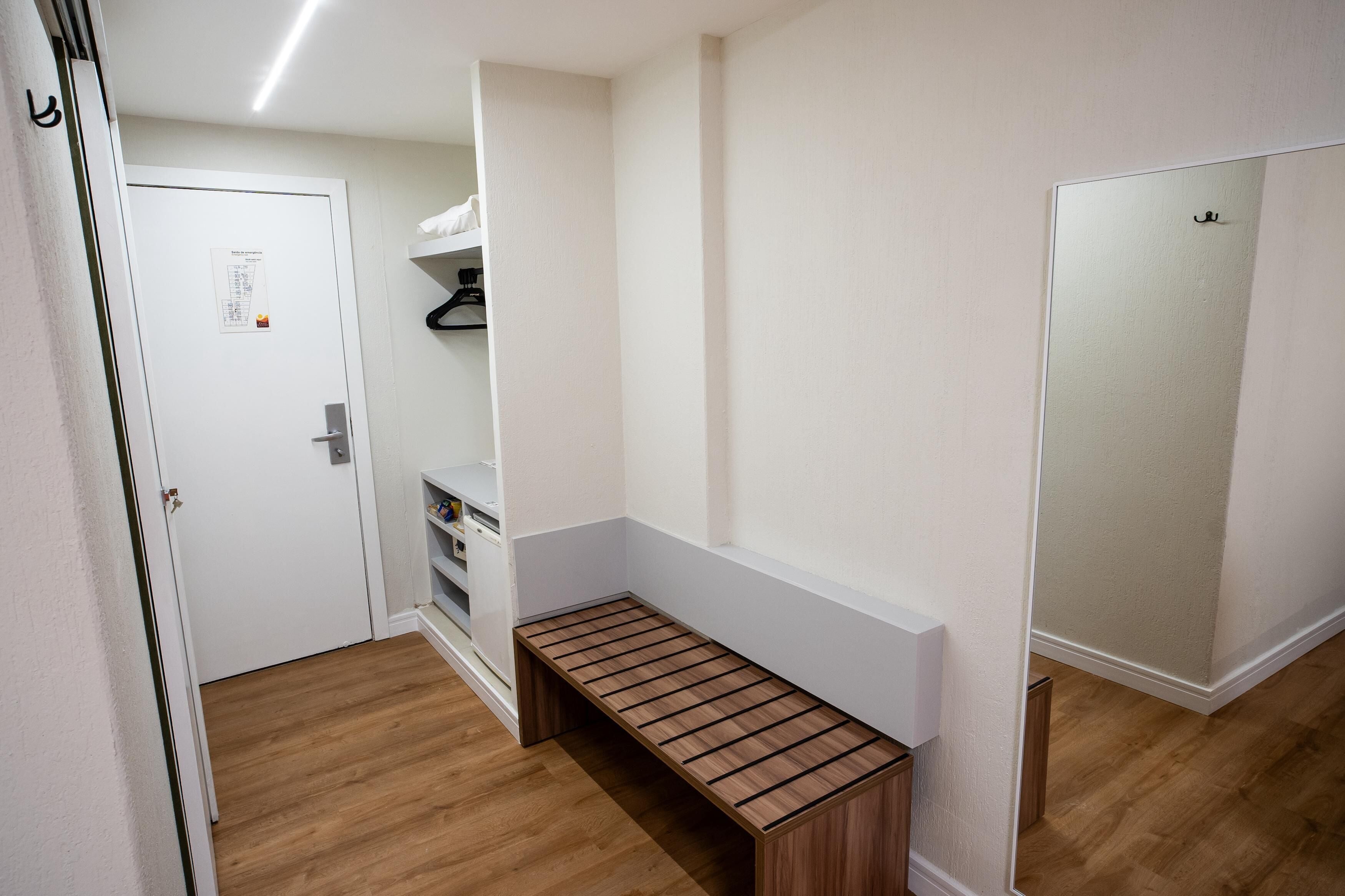 A hallway with a bench, a door with a notice, and a mirror on the wall.