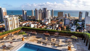 A rooftop pool area with lounge chairs and a swimming pool, overlooking a coastal cityscape with high-rise buildings and a beach. - Hotel Praia Centro (Fortaleza)