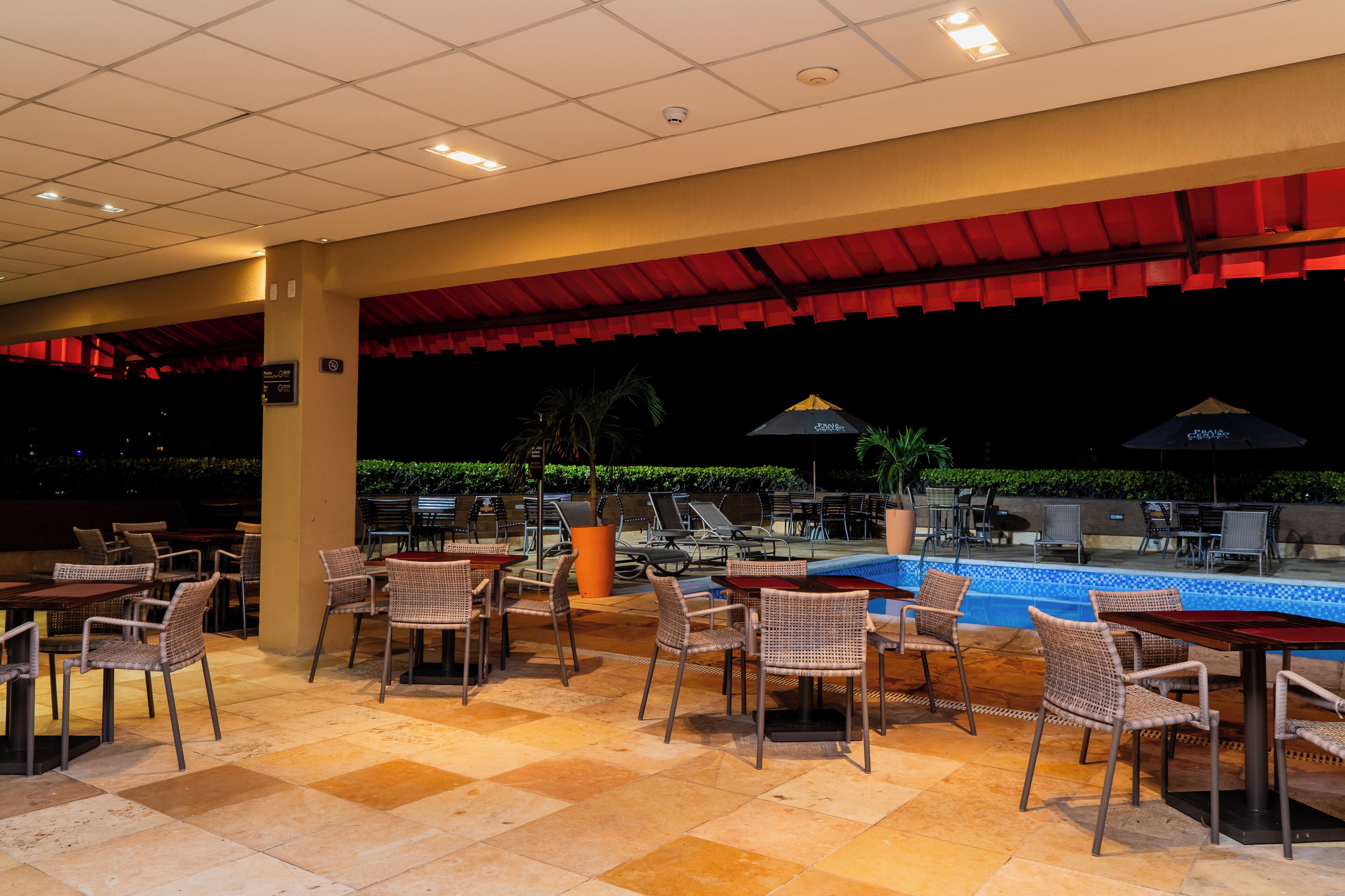 An outdoor patio area with tables and chairs, a swimming pool, and umbrellas.