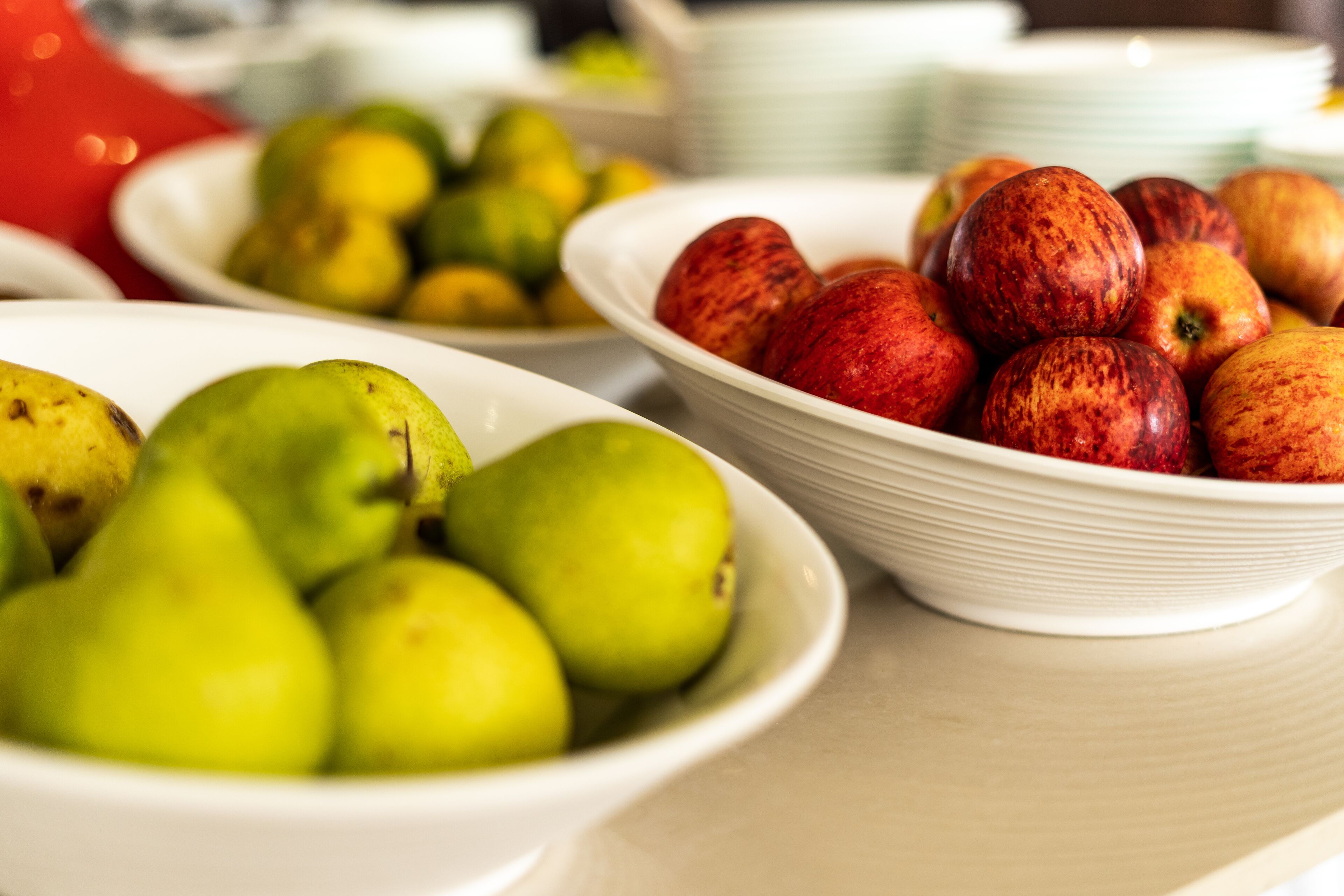 Una mesa con cuencos de peras verdes y manzanas rojas.