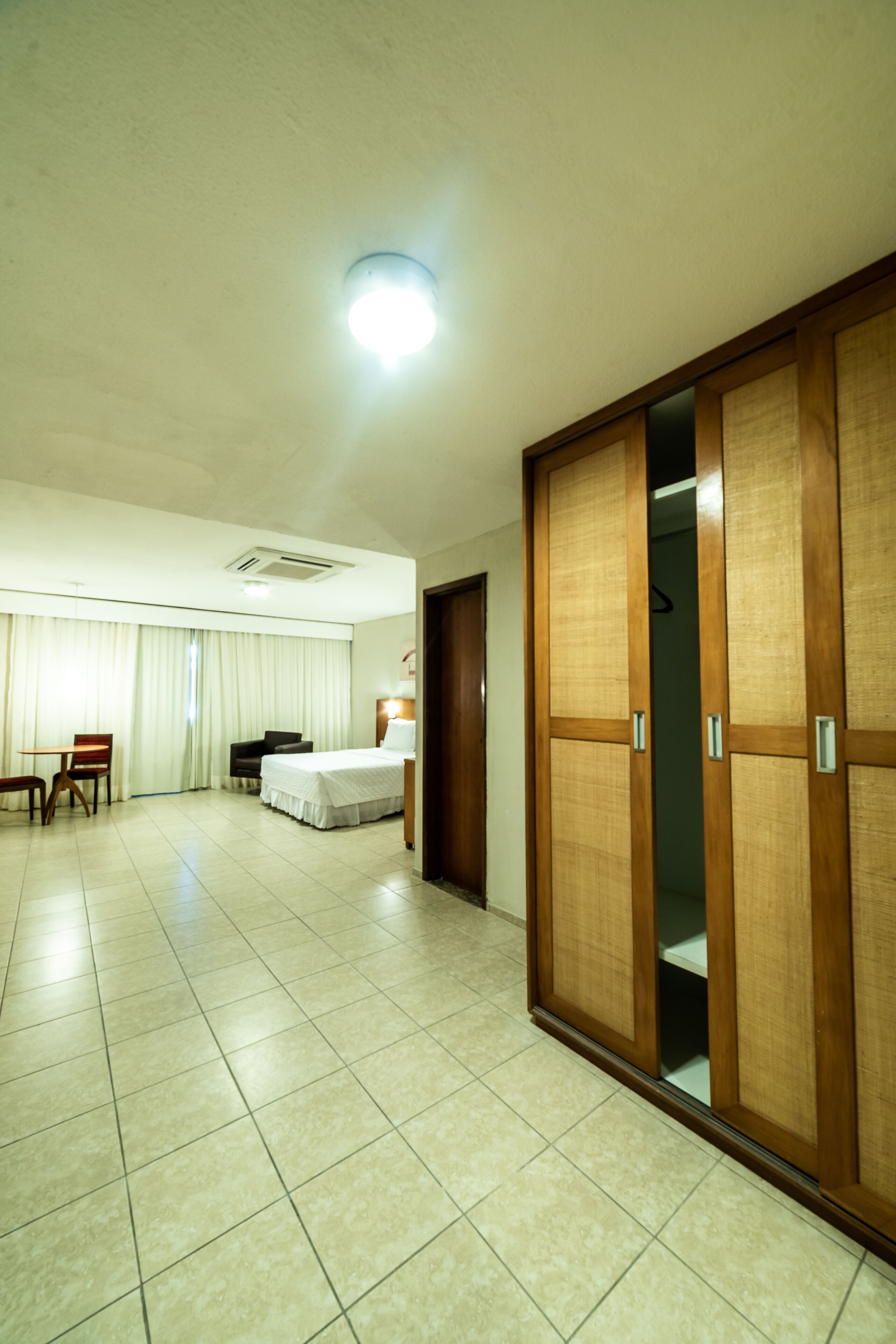 A hotel room with a bed, a desk, a chair, a wardrobe, and a curtain.